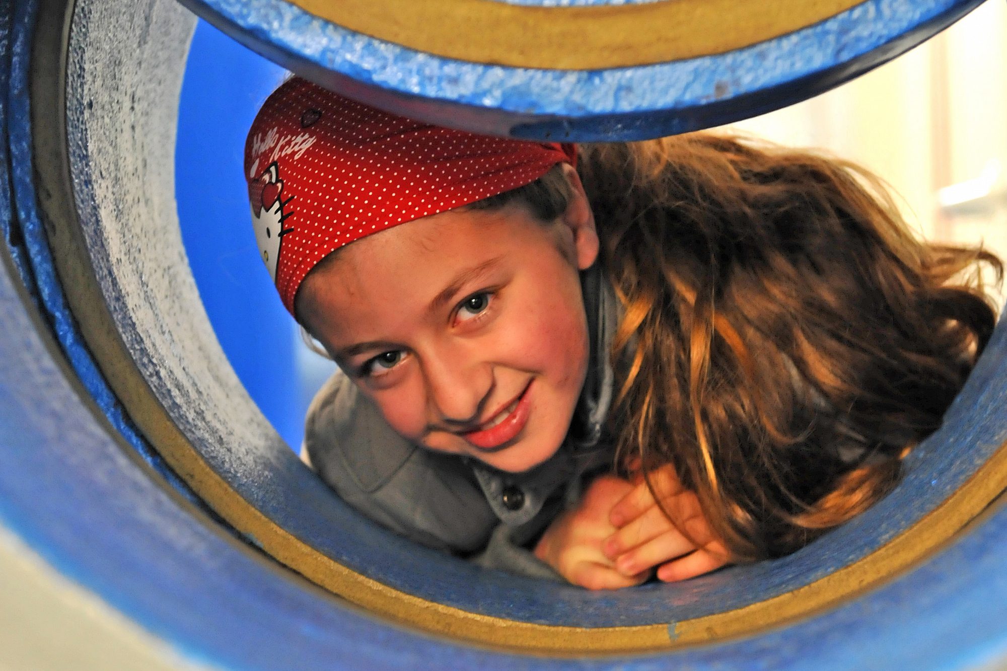 Ein Mädchen liegt in einer großen leeren Wasserleitung auf dem Bauch und schaut lächelnd aus dem Rohr.
